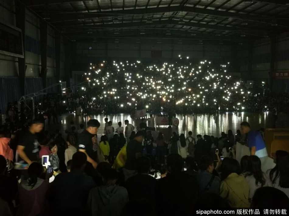 黑暗的篮球馆内，数千名观众高举点亮的手机，无数道白色光束如星光般交织，照亮了球场中央，氛围既神秘又感人