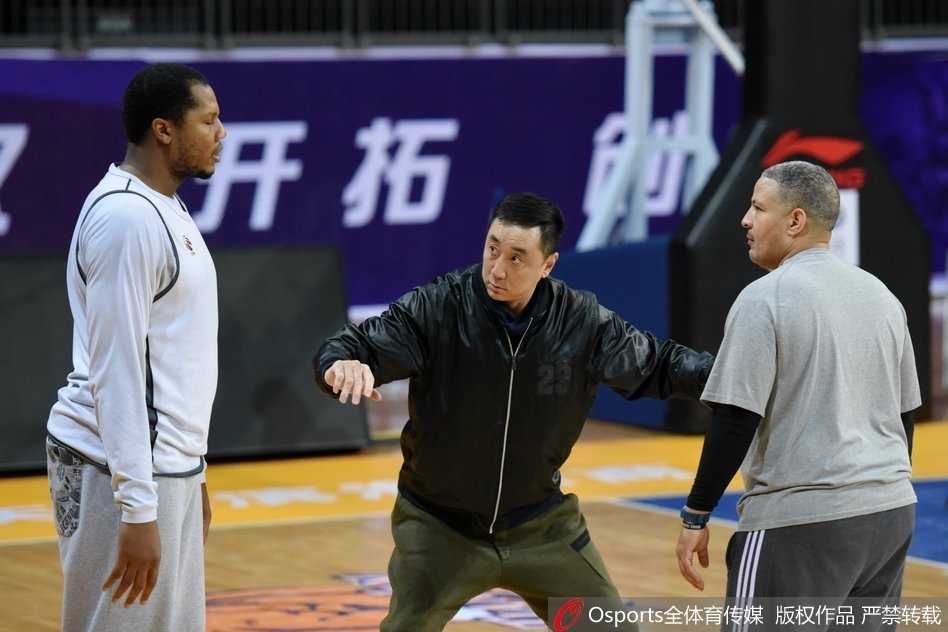 训练结束后，休利与王非在场边促膝长谈，两人面带笑容，身后的球馆灯光映照着这份深厚的篮球情谊。