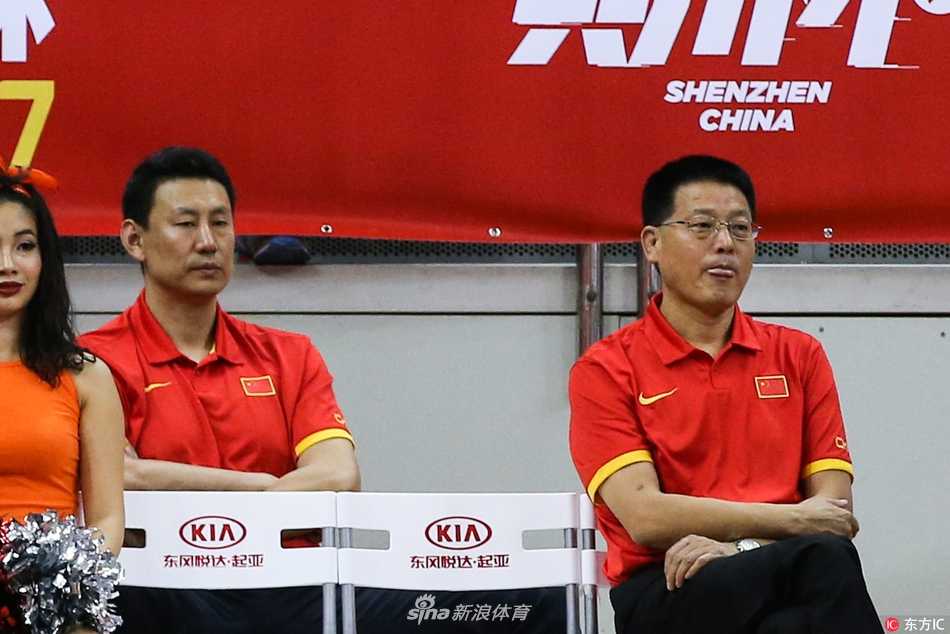 深圳宝安体育馆内灯火通明，身着红色队服的中国队全体成员整齐地坐在场边板凳席上。他们的目光齐刷刷地投向场内，眼神中带着专注与思索，仿佛在拆解着场上欧洲球员的每一个战术跑位。身后看台上，五星红旗在人群中若隐若现，整个画面凝固成一种独特的备战瞬间。