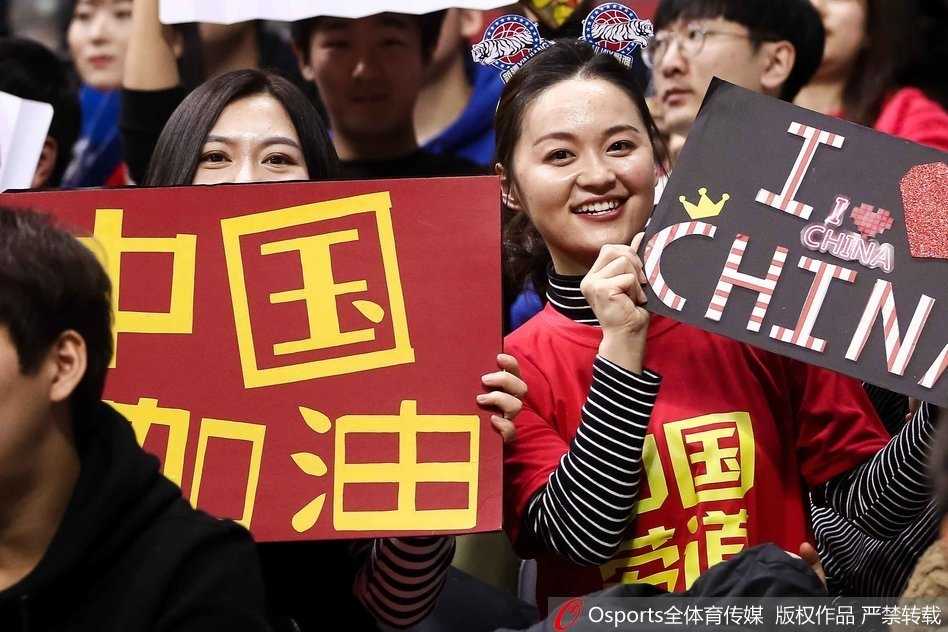 这位长发披肩的女生神情专注地看着场内方向，手中的加油牌上写着鼓舞人心的语句，她安静而坚定的姿态宛如赛场边一道宁静而有力的风景，默默为球员输送着精神力量。