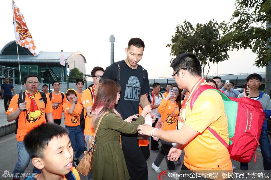 球迷热情接风,华南虎踏上逆袭征途 身穿红色外套的易建联神情专注,正低头为热情的球迷递上的球衣签名,眼神中带着一丝疲惫却满是耐心。