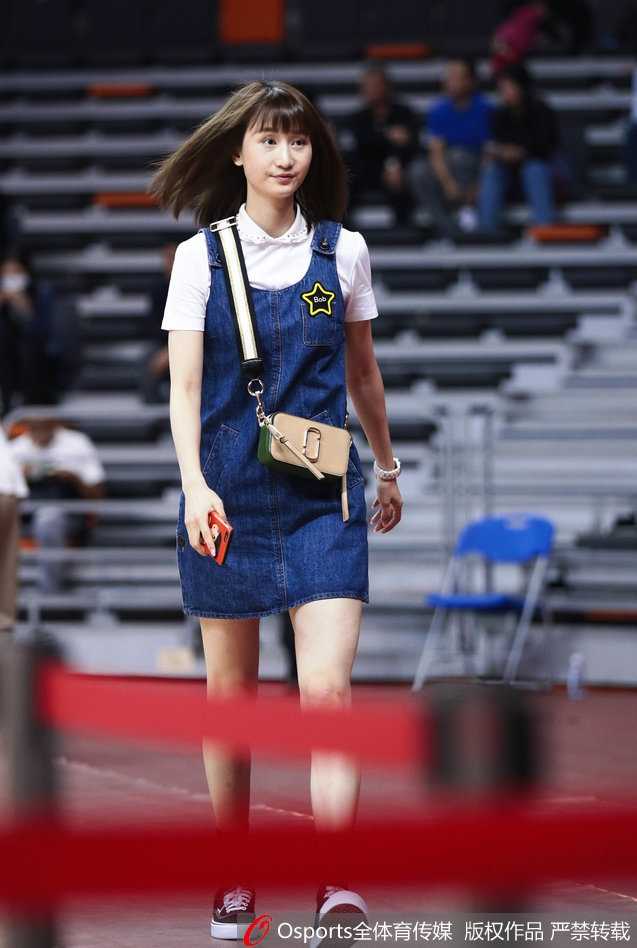 身着牛仔裙的刘美坐在场边观众席上，她专注地望向球场方向，一双修长的美腿在灯光下显得格外吸睛，仿佛将T台搬到了篮球赛场。