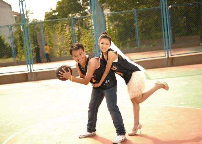 新郎从背后温柔环抱坐在罚球线上的新娘，两人手中共同托举着一颗篮球，背景的篮球架和看台都成了他们纯粹爱情的沉默见证者。