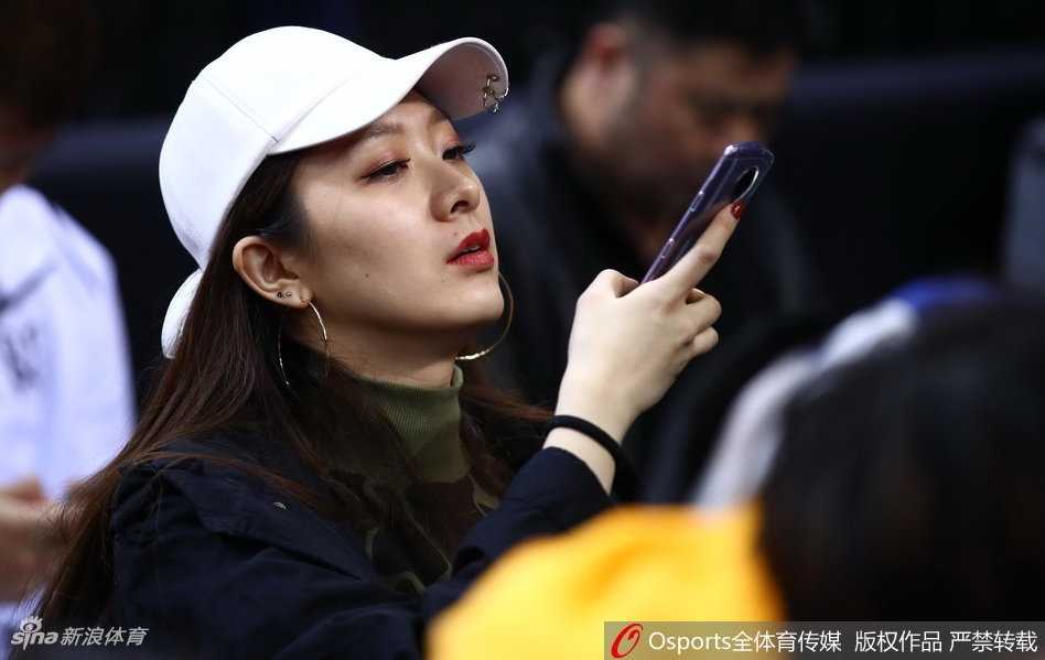 翟晓川与妻子杨思雨坐在CBA全明星赛场边，两人都穿着深色系休闲装，神情专注地看着场内激烈的星锐赛，偶尔低声交流，眼神中满是默契与温情。