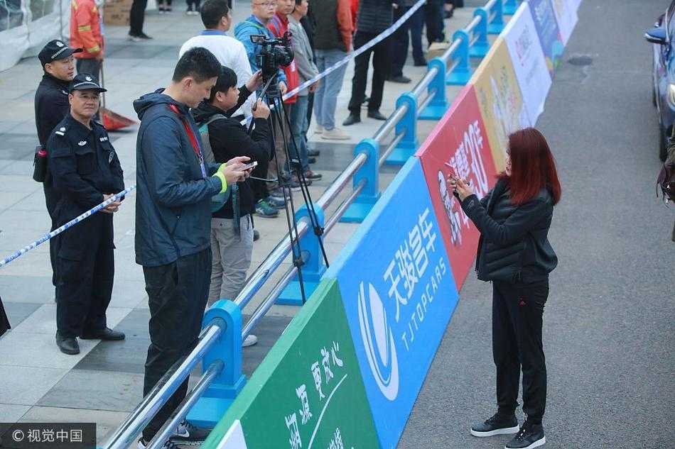 莞马赛场边的温情一幕:冬日娜与杜锋互加好友 镜头拉远,冬日娜和杜锋并肩站在赛道旁的护栏边,周围是攒动的人头和飘扬的旗帜。完成扫码的两人似乎正进行着简短的交流,身后巨大的赛事背景板无声地宣告着这场亚洲田径盛事的主场。