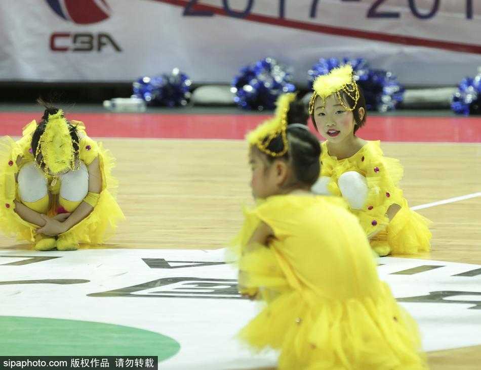 两名萌娃面对面站立，她们穿着统一的红色表演服，像是在相互鼓励或交流动作，稚拙的身高差和懵懂的表情让这一刻显得格外温馨可爱。