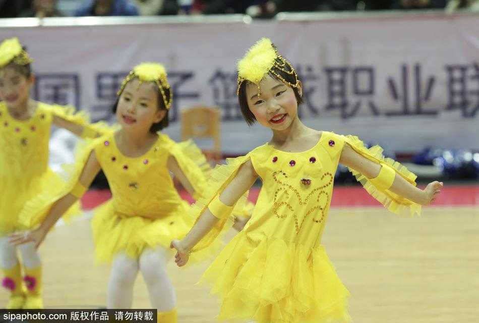 几名小队员站成一排，手里拿着色彩鲜艳的花球，背景是巨大的CBA赛场广告牌。她们在等待退场，眼神中带着好奇与一丝疲惫，但依然紧紧抱着花球，舍不得放下。