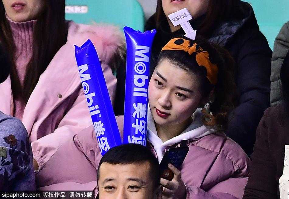 一名身穿深色V领上衣的女球迷正在低头查看手机，也许是在和朋友分享此刻激动的心情，又或是查看本场比赛的技术统计。即使是低头的瞬间，她精致的侧脸和柔顺的长发依然构成了一幅美好的画面。