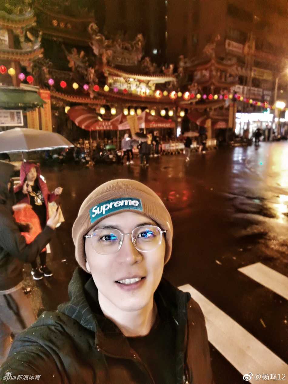 杨鸣与台北街头的特色招牌合影，面带微笑，心情极佳。背景中的繁体字广告牌和穿梭的人群，记录下这位CBA帅哥在宝岛留下的又一帅气瞬间。