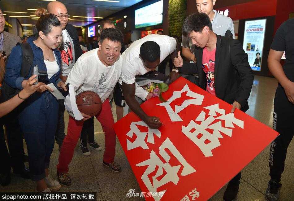 机场大厅内，巴斯一边拖着行李前行，一边不忘回头与身旁的球迷挥手致意，举手投足间尽显亲和力。