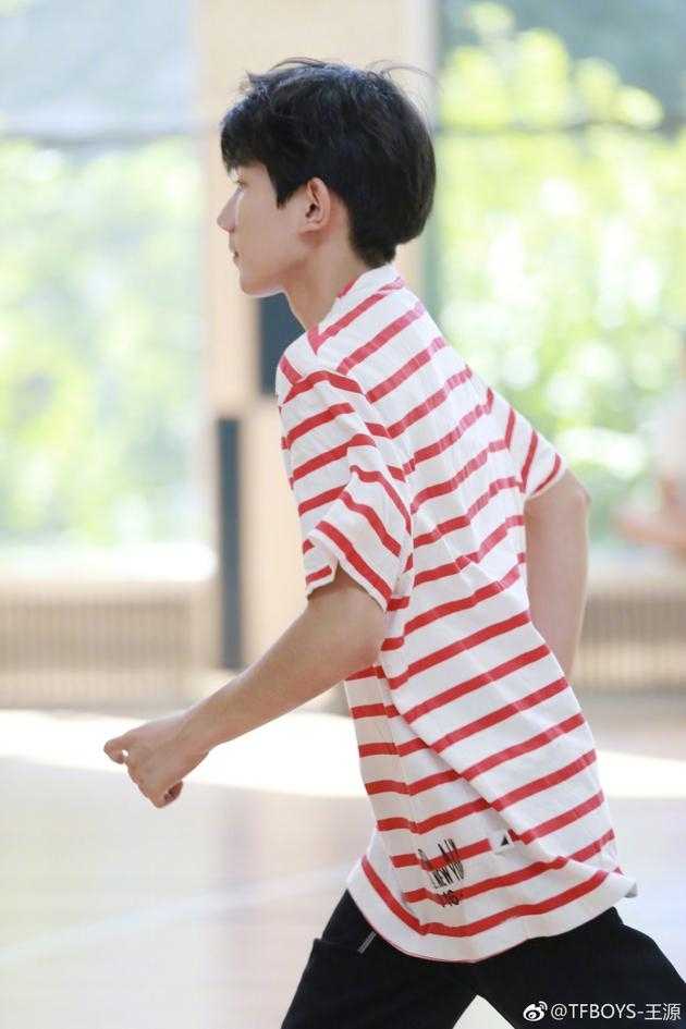 王源在篮筐下回眸一笑，阳光透过条纹衫映出斑驳光影，黑色裤脚随动作轻扬，整个人像镀上一层青春的金边